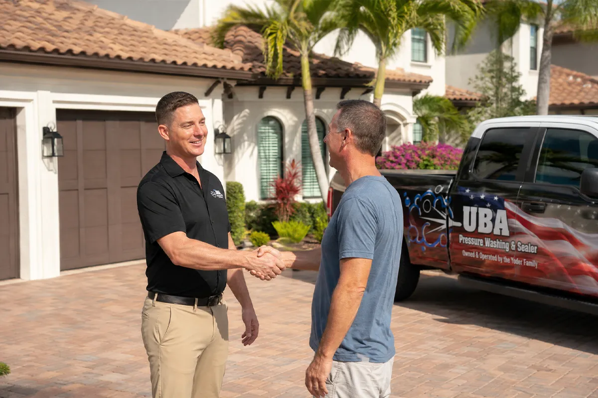 UBA Pressure Washing owner shaking hands with a satisfied Sarasota homeowner in front of the branded UBA service truck on a sealed paver driveway