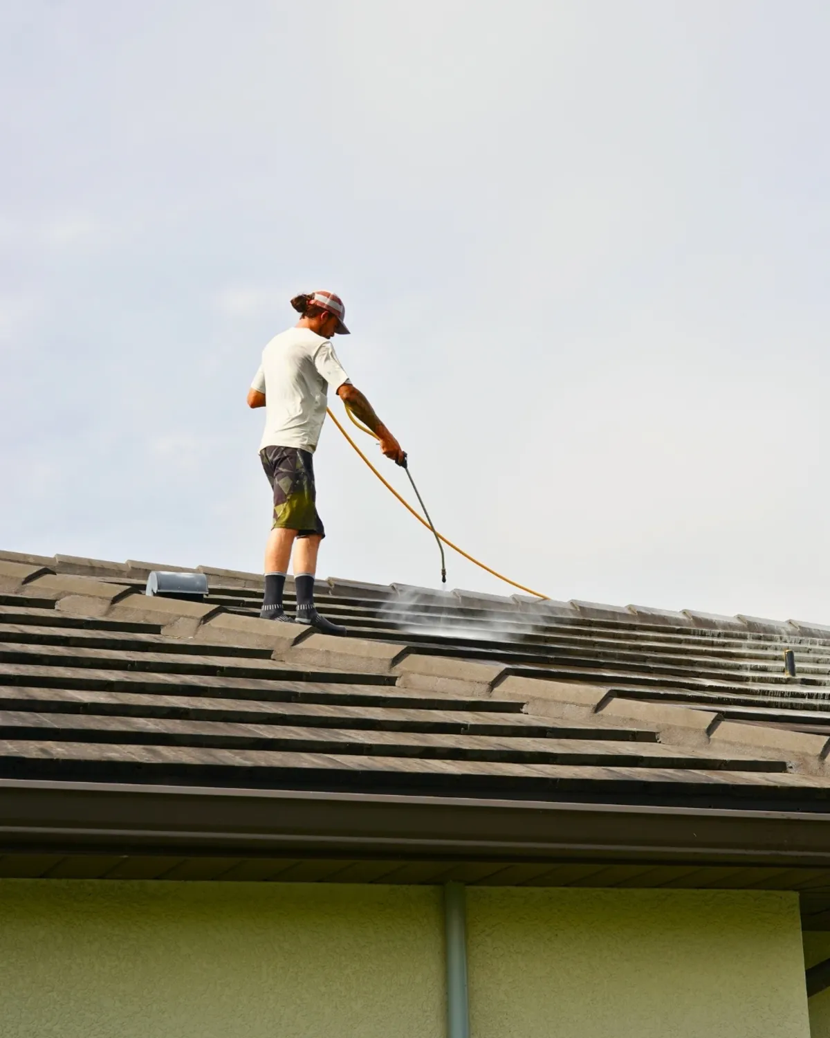 UBA technician standing on a Florida flat tile roof applying low-pressure soft wash solution with a spray wand, demonstrating the safe chemical cleaning method UBA uses on all Sarasota tile roofs