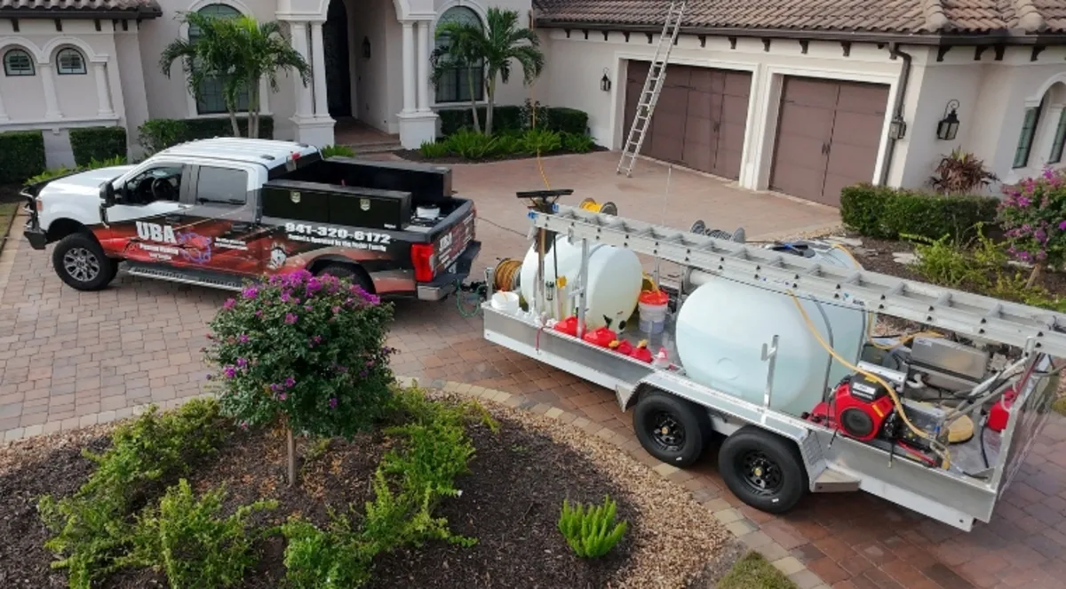 Aerial view of UBA Pressure Washing branded truck and custom aluminum equipment trailer parked in the paver driveway of a luxury Sarasota home, showing the professional equipment setup UBA brings to every job