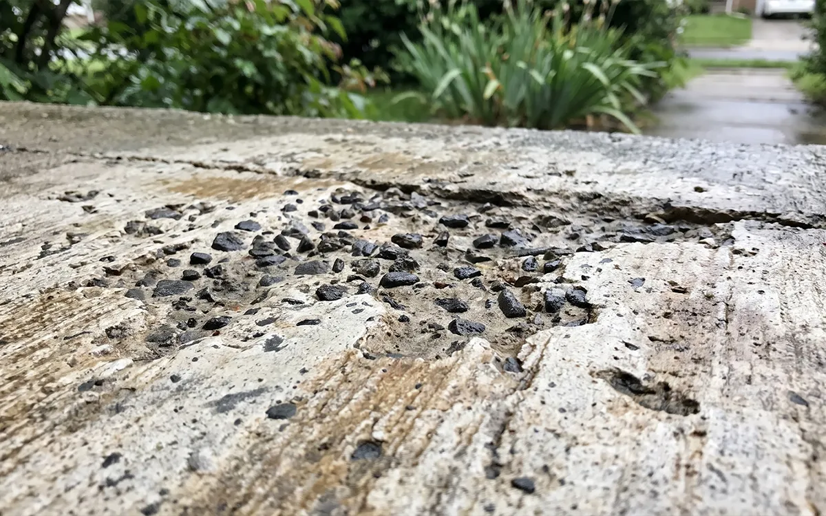 Close-up of a Sarasota sidewalk showing concrete damaged by high-pressure washing, rougher aggregate exposed where the cement paste layer has been stripped away