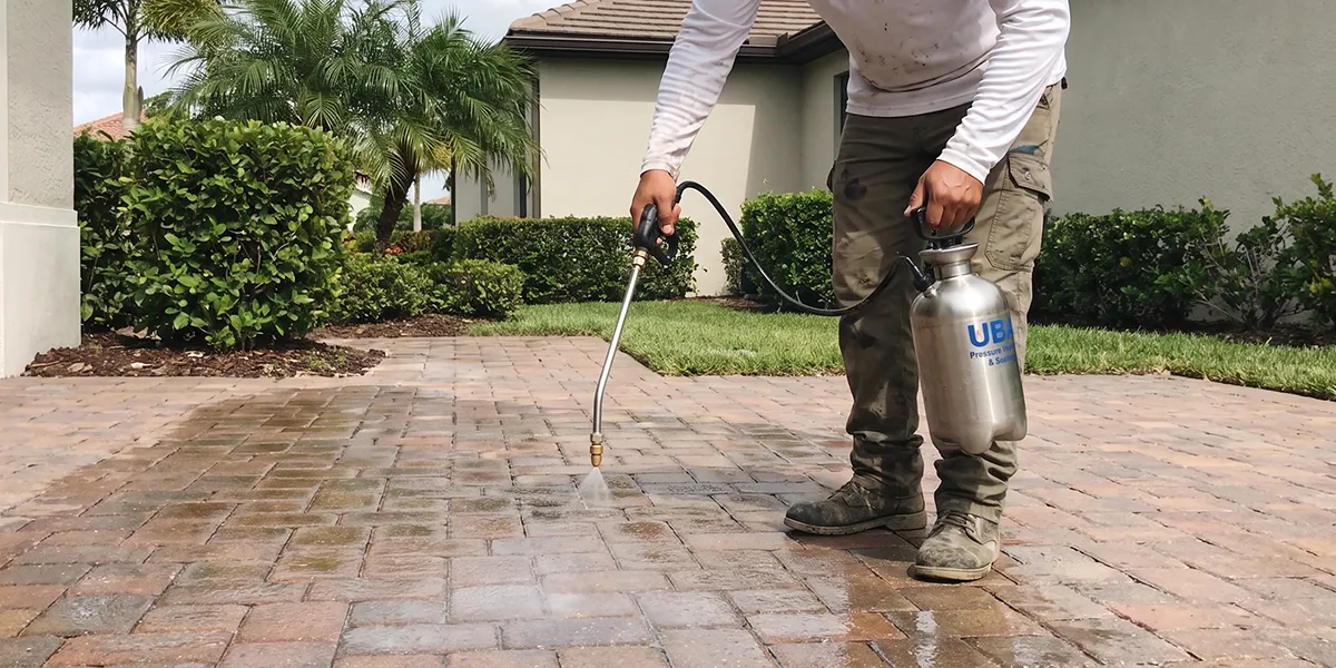 UBA crew member applying sealer to a paver walkway with a pump sprayer in a Sarasota community